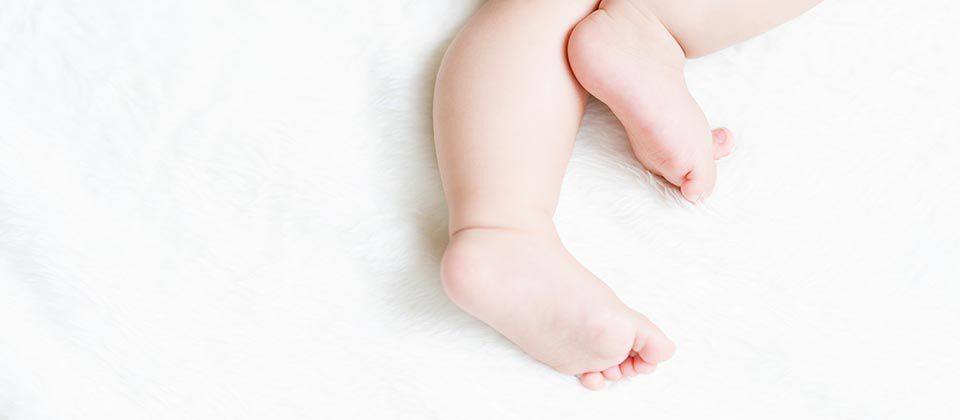A close-up of a baby's feet and legs resting on a soft, fluffy white surface.