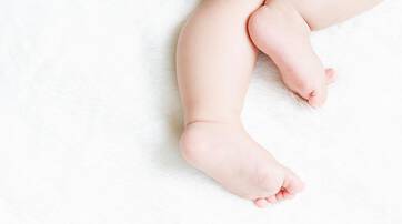 A close-up of a baby's feet and legs resting on a soft, fluffy white surface.