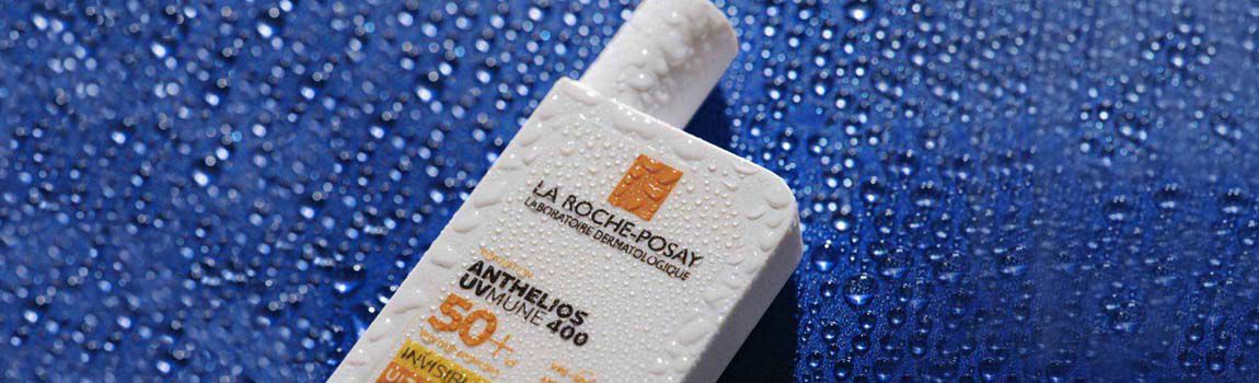 A bottle of La Roche-Posay Anthelios sunscreen with water droplets on it, sitting against a blue background.