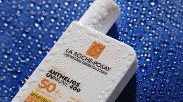 A bottle of La Roche-Posay Anthelios sunscreen with water droplets on it, sitting against a blue background.