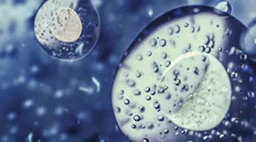 Close-up of spherical droplets in varying sizes, with a blurred blue background, creating a sense of depth and texture.