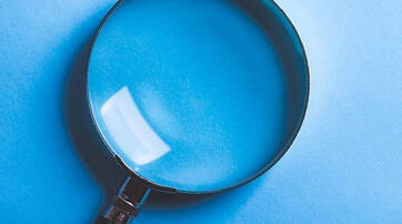 A large magnifying glass resting on a light blue surface.