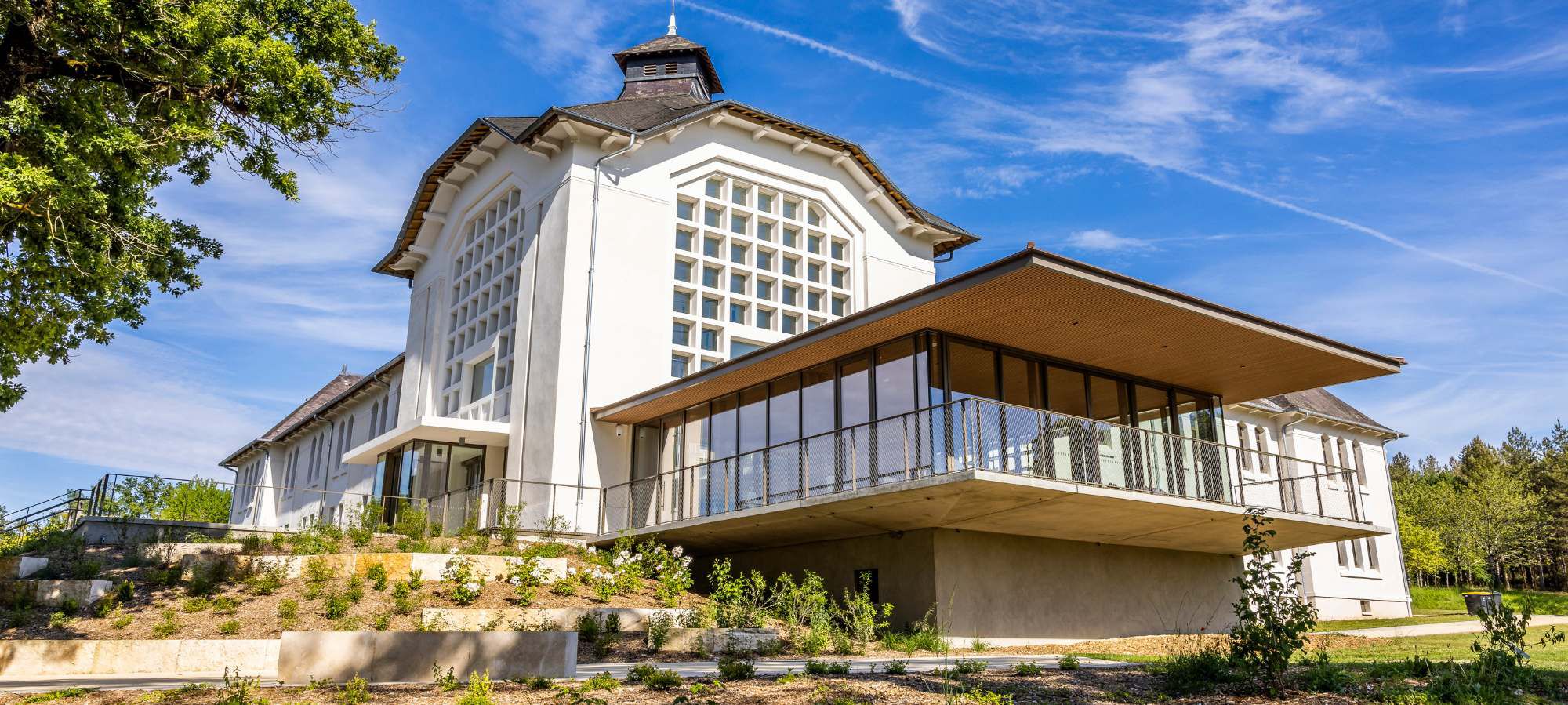 A modern building with a large glass front surrounded by greenery, labeled "Thermes du Connetable," under a clear blue sky.