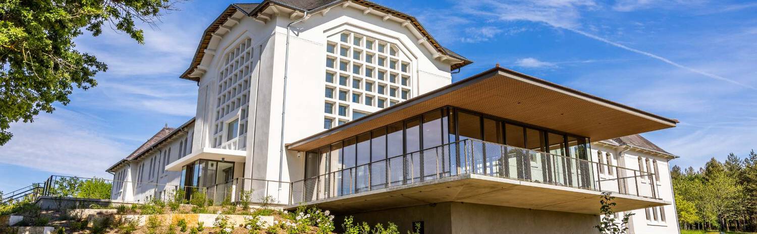A modern building with a large glass front surrounded by greenery, labeled "Thermes du Connetable," under a clear blue sky.