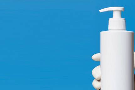 Flacon pompe blanc tenu par une main sur un fond bleu.