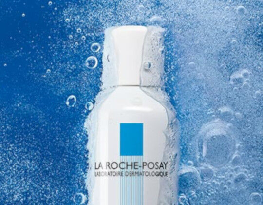 A white bottle of La Roche-Posay skincare product surrounded by blue water droplets.