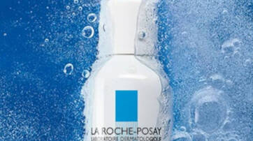 A white bottle of La Roche-Posay skincare product surrounded by blue water droplets.