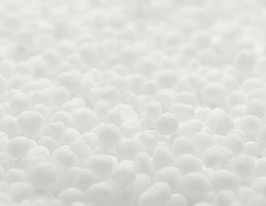 A close-up image of numerous small, white spherical objects resembling small beads or pellets, arranged densely against a soft, blurred background.