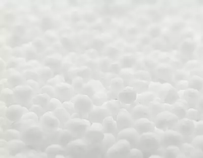 A close-up image of numerous small, white spherical objects resembling small beads or pellets, arranged densely against a soft, blurred background.