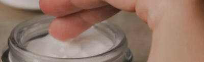 A hand reaching into a jar of cream, with a small amount of the white cream on the fingertip.