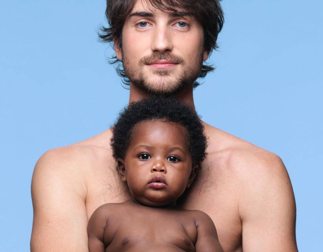 Un homme portant un bebe sur ses bras, tous deux exposes sur un fond bleu.