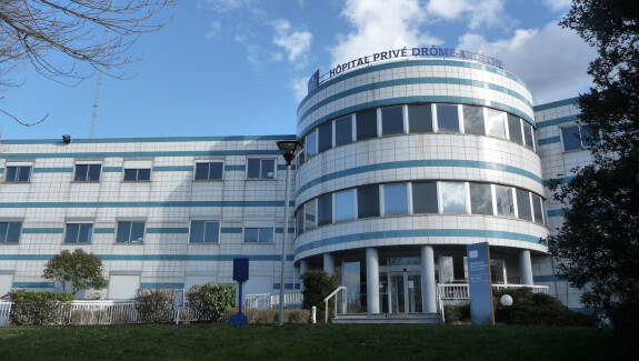 Hopital prive Drome, batiment moderne avec facade en verre et ciel nuageux.