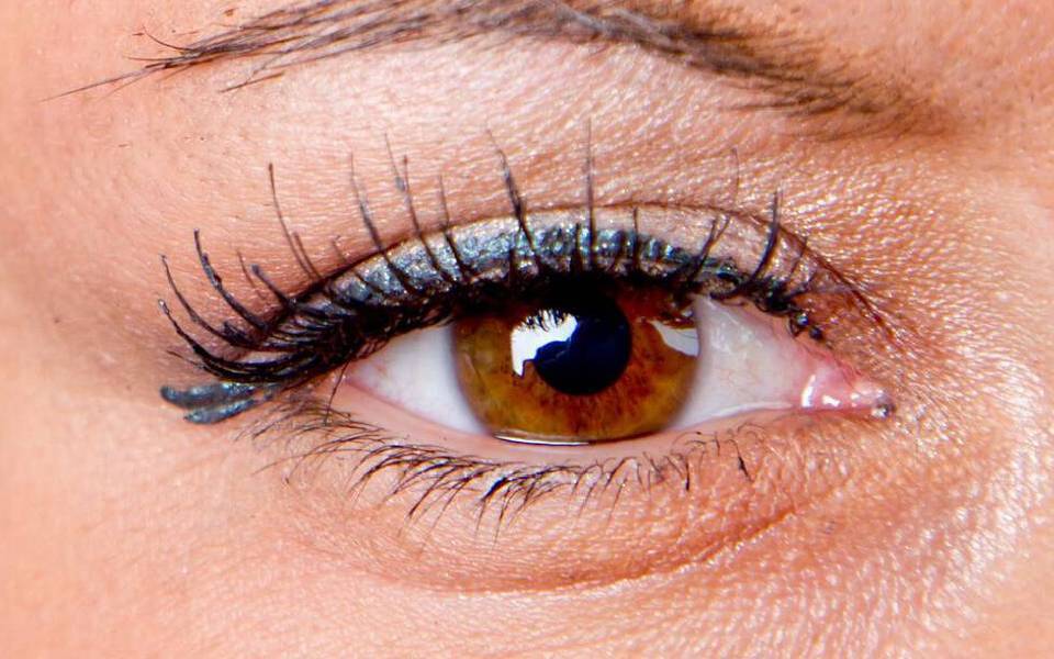 Un gros plan sur un oeil brun avec un maquillage subtil, le regard expressif, sur fond noir.