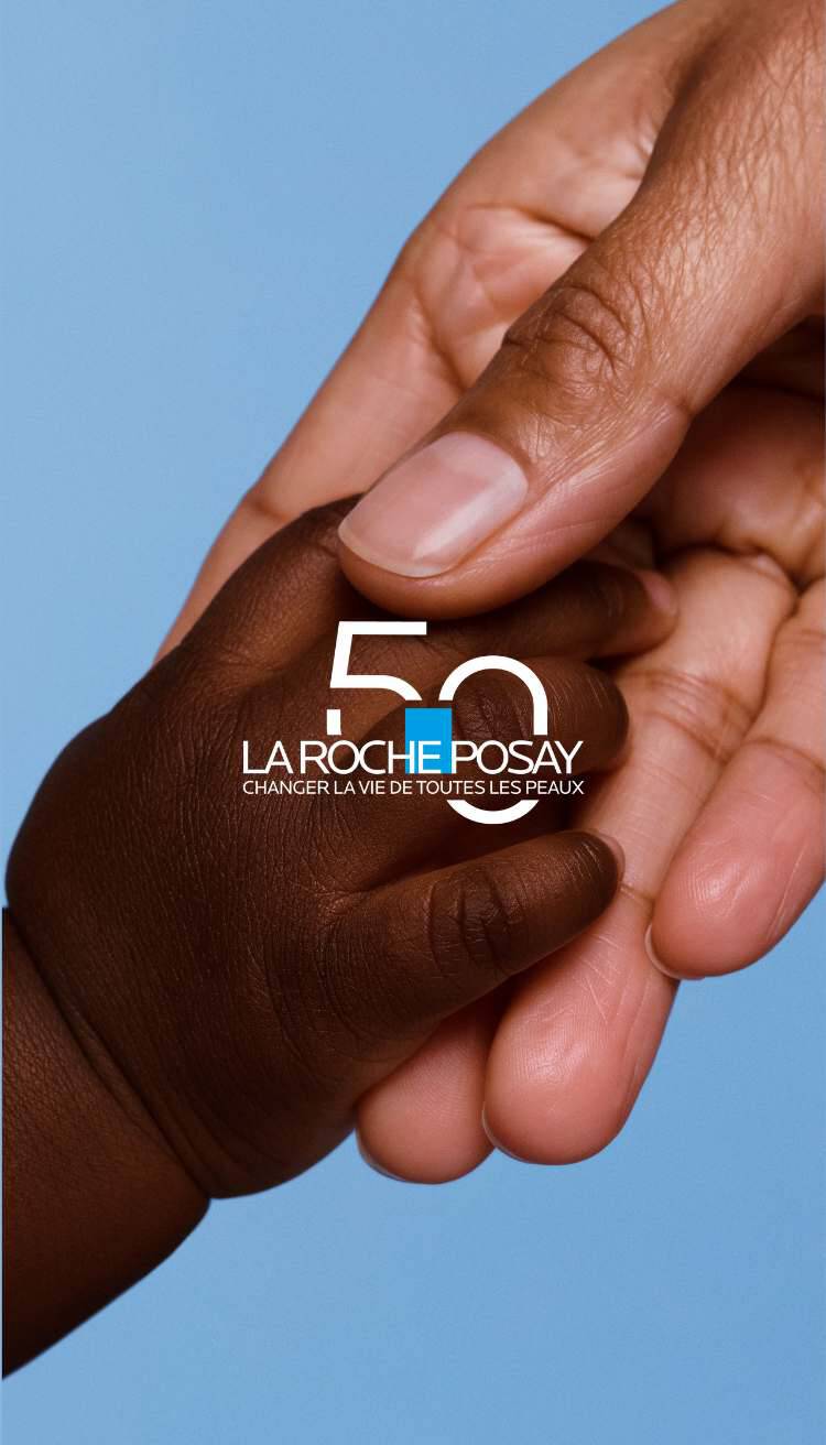 Une main adulte tenant une petite main d'enfant, avec le logo de La Roche-Posay et le texte "50" sur fond bleu.