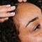 A close-up of a person with curly hair receiving a scalp massage, with a hand gently touching their forehead. The person has freckles and appears relaxed.
