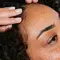 A close-up of a person with curly hair receiving a scalp massage, with a hand gently touching their forehead. The person has freckles and appears relaxed.