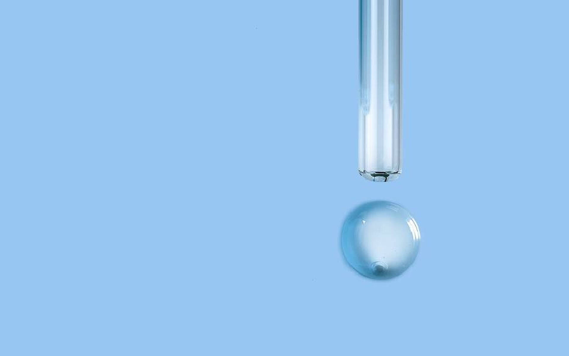 Une pipette au-dessus d'une goutte d'eau sur fond bleu.