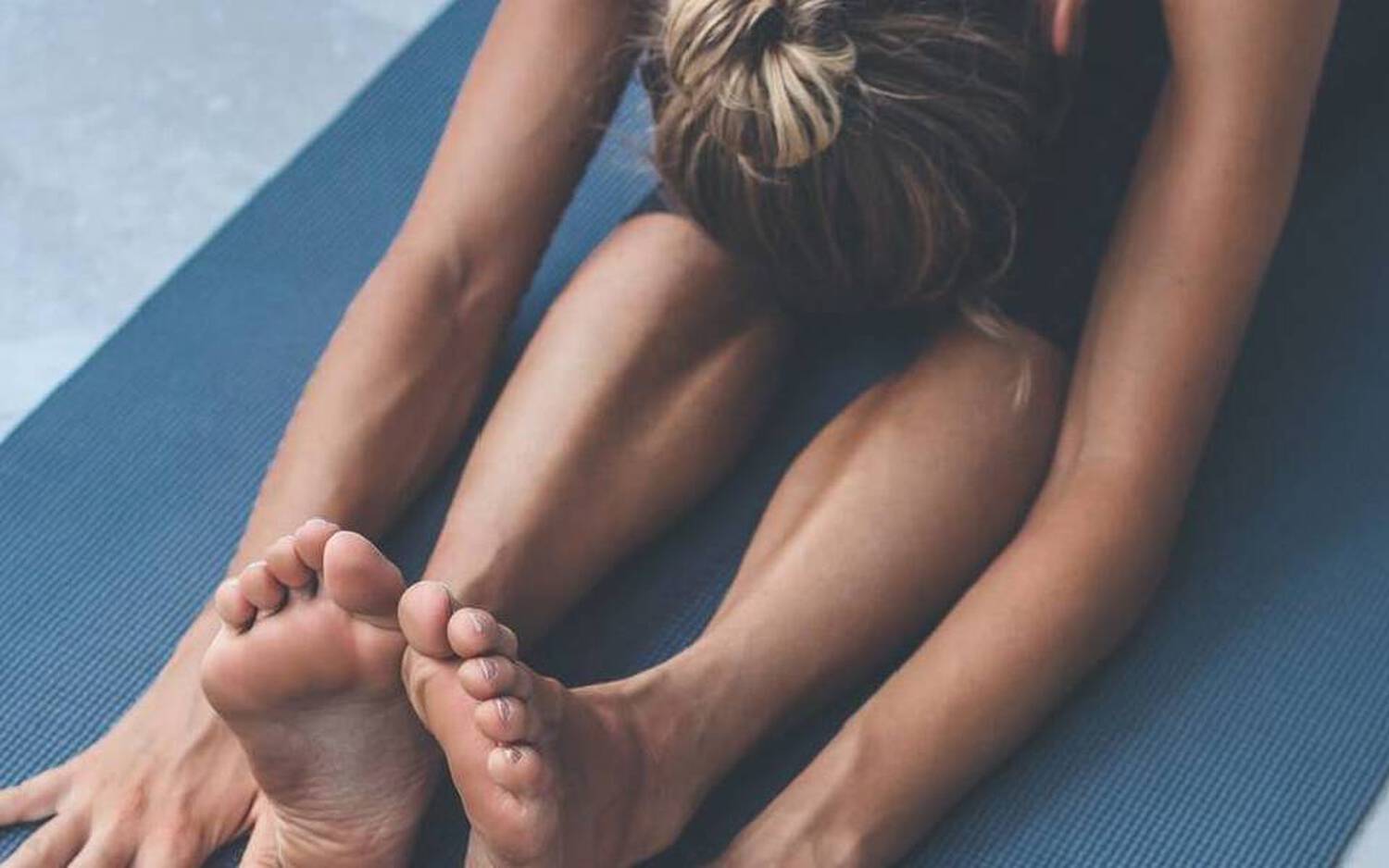 Une personne pratique des etirements sur un tapis de yoga, allongee vers l'avant, atteignant ses pieds.