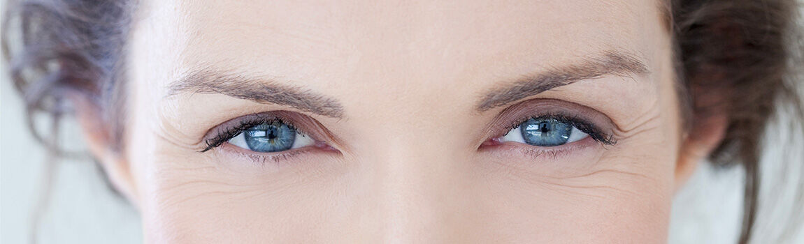 Close-up of a person's eyes, showcasing blue irises and well-defined eyelashes. The skin around the eyes shows fine lines, adding to the expressive appearance.