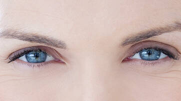 Close-up of a person's eyes, showcasing blue irises and well-defined eyelashes. The skin around the eyes shows fine lines, adding to the expressive appearance.