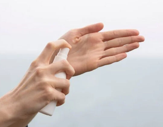 Une main tenant un flacon pulverisateur, appliquant un produit sur l'autre main.