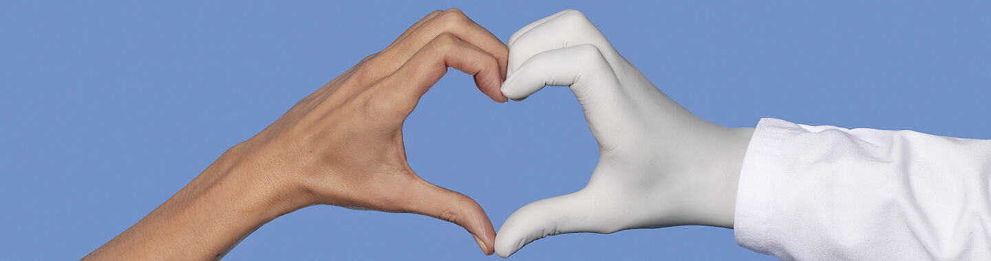 Une main nue et une main portant un gant medical blanc formant ensemble un coeur sur un fond bleu.
