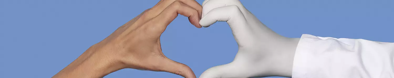 Une main nue et une main portant un gant medical blanc formant ensemble un coeur sur un fond bleu.