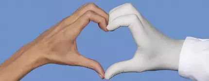 Une main nue et une main portant un gant medical blanc formant ensemble un coeur sur un fond bleu.