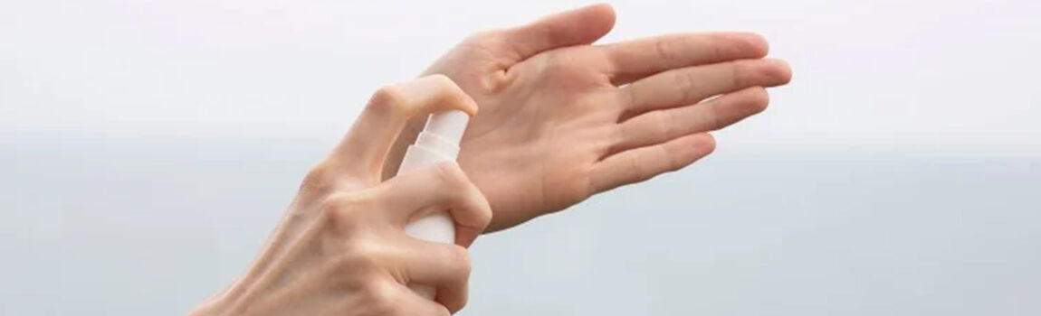 Un close-up d'une main pulverisant un produit sur l'autre main, avec un arriere-plan flou d'eau.