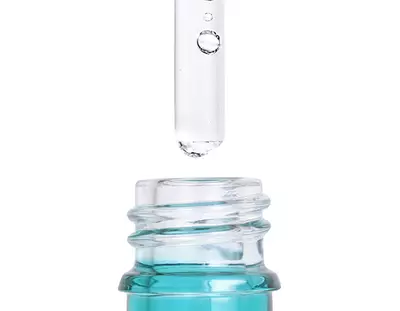 Une pipette liberant une goutte au-dessus d'un flacon en verre transparent rempli d'un liquide bleu.