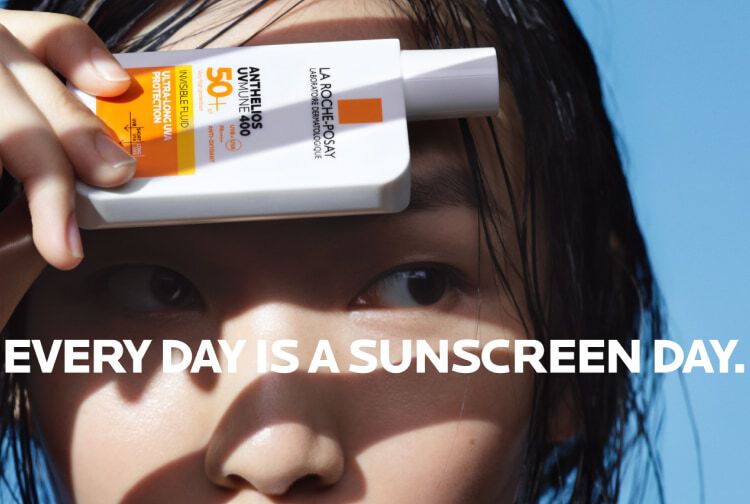 Une personne tient un flacon de creme solaire La Roche-Posay avec un fond bleu.