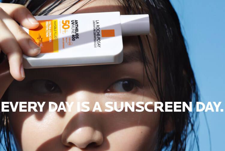 Une personne tient un flacon de creme solaire La Roche-Posay avec un fond bleu.