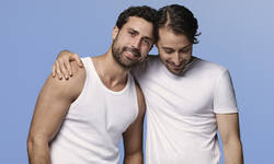 Deux hommes en hauts blancs, souriants et s'enlacant sur un fond bleu clair.