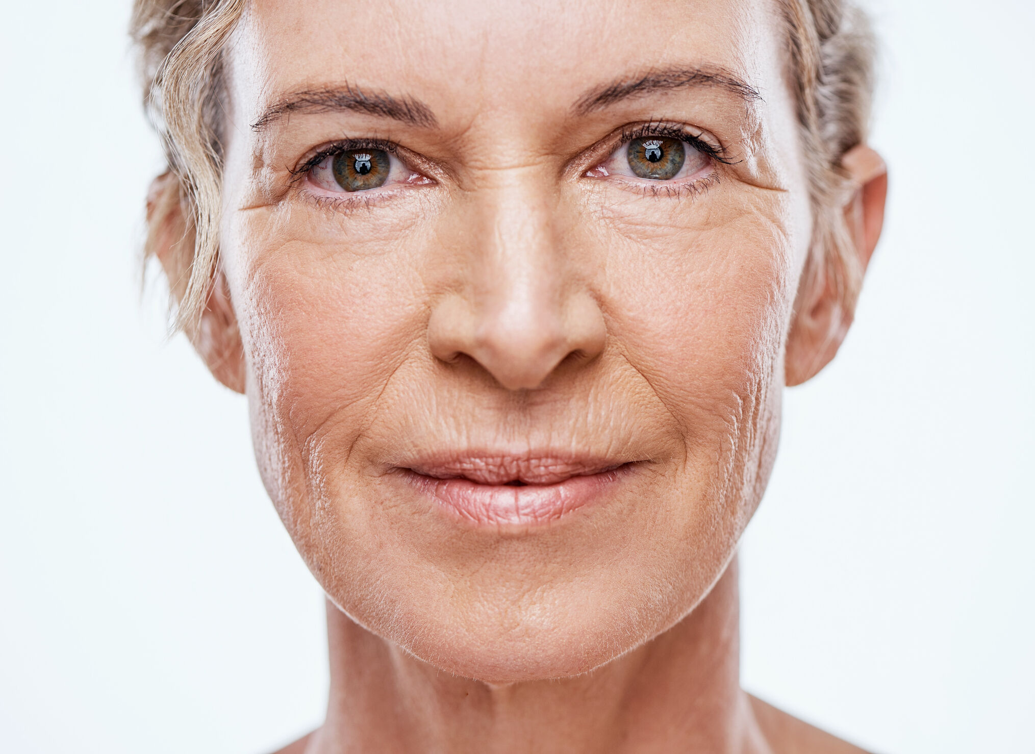 Un portrait en gros plan du visage d'une femme d'age mur, mettant en evidence la texture naturelle de la peau, les ridules et les rides autour des yeux et de la bouche.