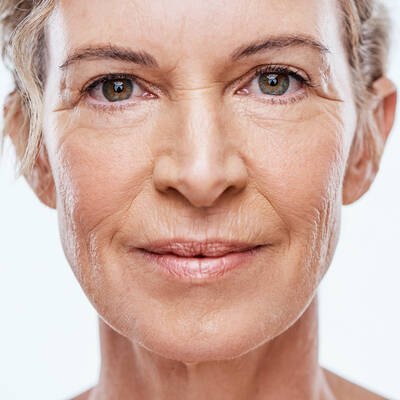 Un portrait en gros plan du visage d'une femme d'age mur, mettant en evidence la texture naturelle de la peau, les ridules et les rides autour des yeux et de la bouche.