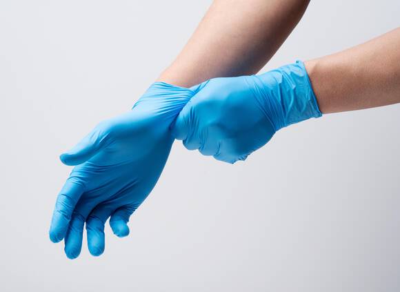 Une main met des gants en latex bleu, illustrant des mesures d'hygiene.