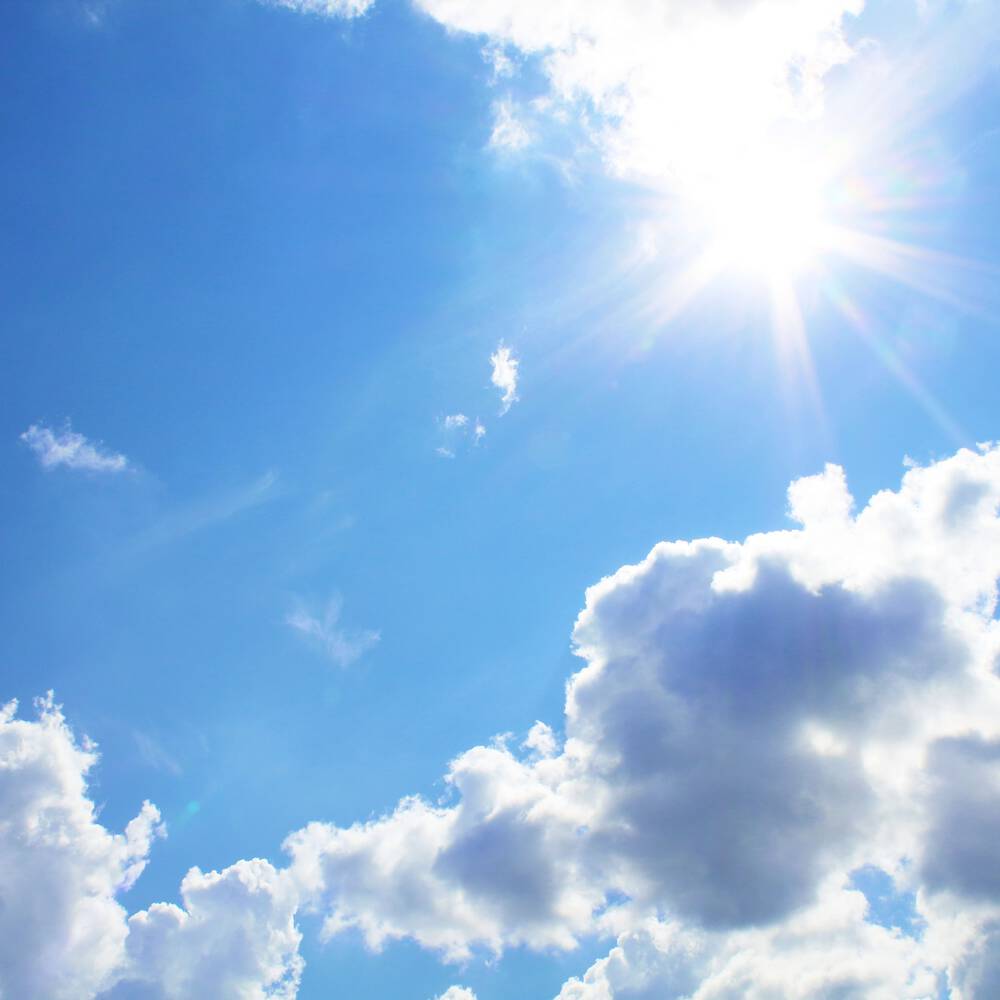 Un ciel bleu parseme de nuages blancs et lumineux, avec un soleil eclatant.