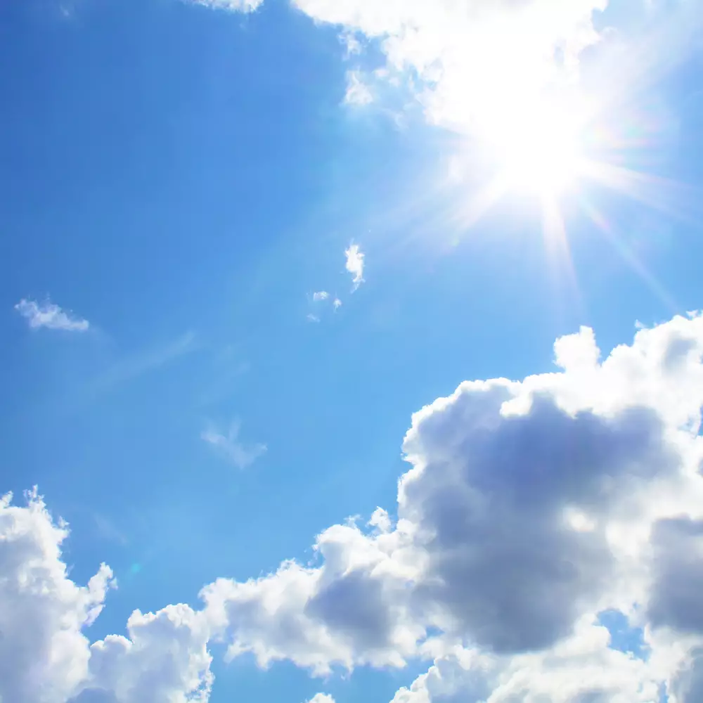 Un ciel bleu parseme de nuages blancs et lumineux, avec un soleil eclatant.