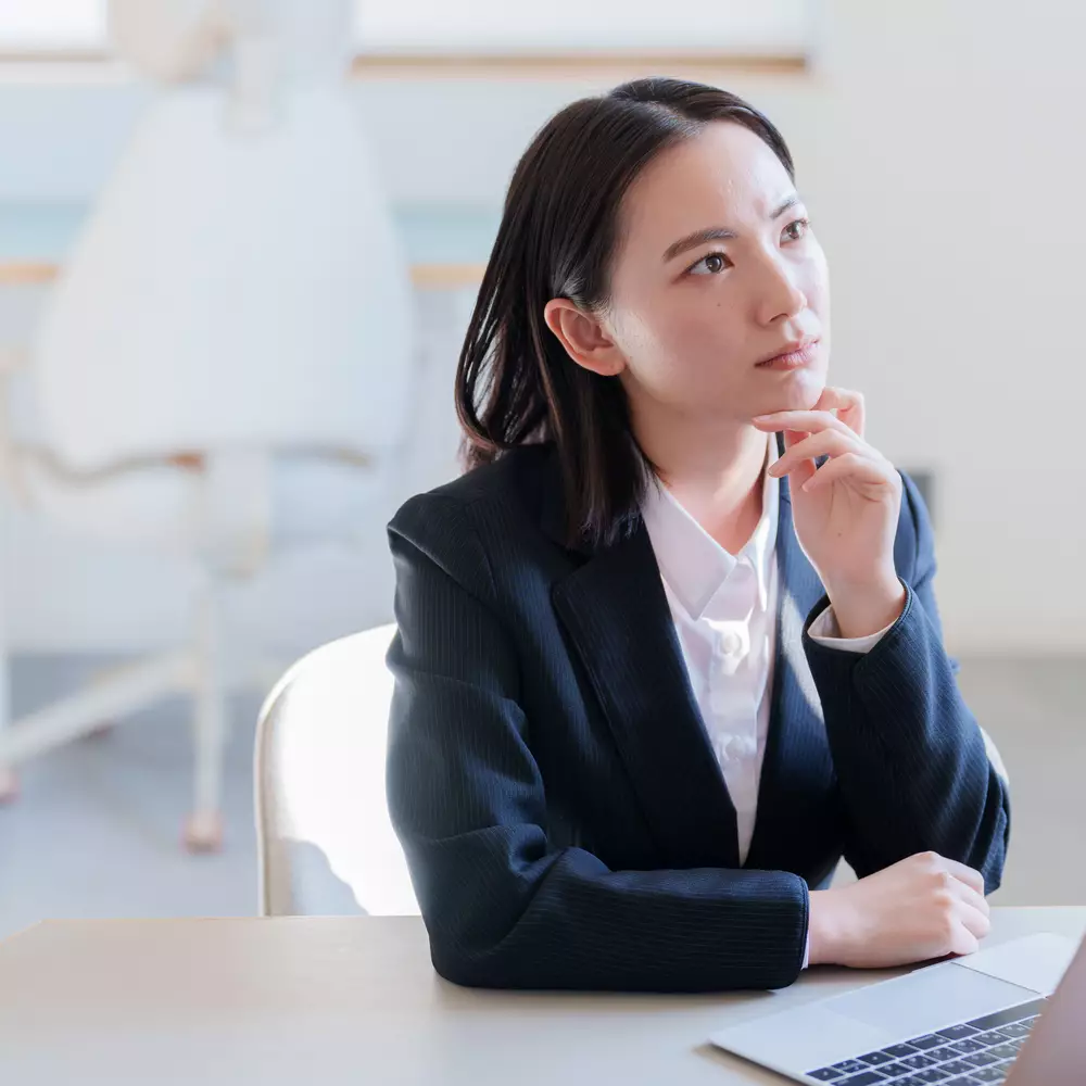 Une femme d'affaires pensive, assise a une table avec un ordinateur portable, regardant au loin.