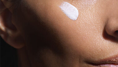 Gros plan sur la joue d'une personne avec une noisette de creme blanche appliquee sur la peau.