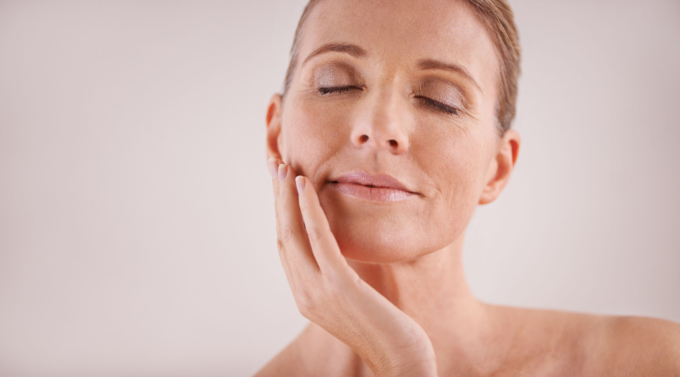 Portrait d'une femme sereine touchant son visage avec douceur, mettant en avant une peau eclatante.