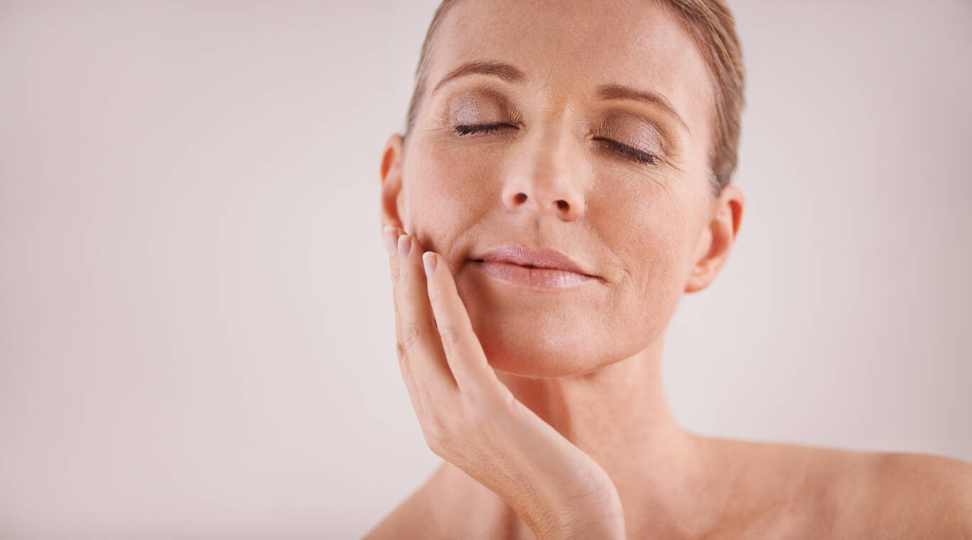 Portrait d'une femme sereine touchant son visage avec douceur, mettant en avant une peau eclatante.