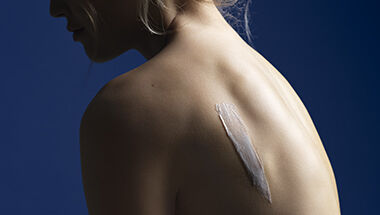 Gros plan sur le dos nu d'une personne avec une trace de creme blanche appliquee sur la peau, sur un fond bleu fonce.