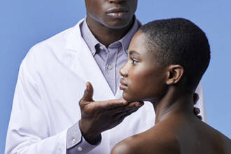 Un dermatologue en blouse blanche examinant le cou et la machoire d'une jeune femme sur un fond bleu.