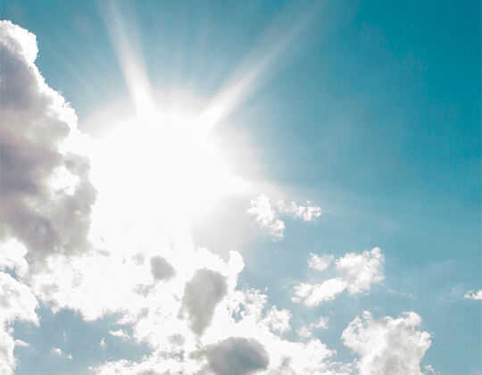Un ciel bleu clair avec un soleil brillant emettant des rayons de lumiere au-dessus de quelques nuages.