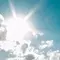 Un ciel bleu clair avec un soleil brillant emettant des rayons de lumiere au-dessus de quelques nuages.