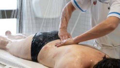 Un soin d'hydrotherapie ou les mains d'un therapeute massent le dos d'une personne sous de fins jets d'eau.