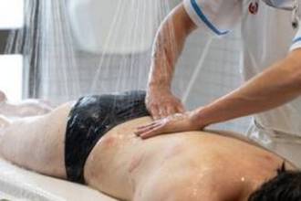 Un soin d'hydrotherapie ou les mains d'un therapeute massent le dos d'une personne sous de fins jets d'eau.