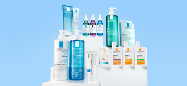 Gamme de soins de peau avec plusieurs flacons et tubes blancs et bleus, présentés entre deux mains stylisées.